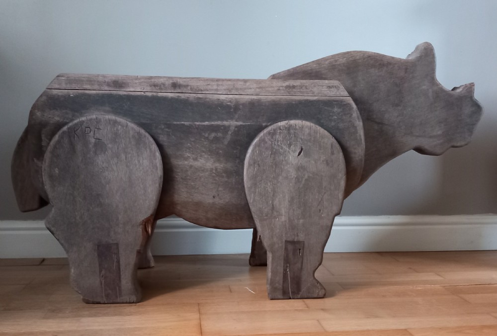 A carved solid oak bench shaped like a rhinoceros with a flat back seat and a dark timber finish. View II