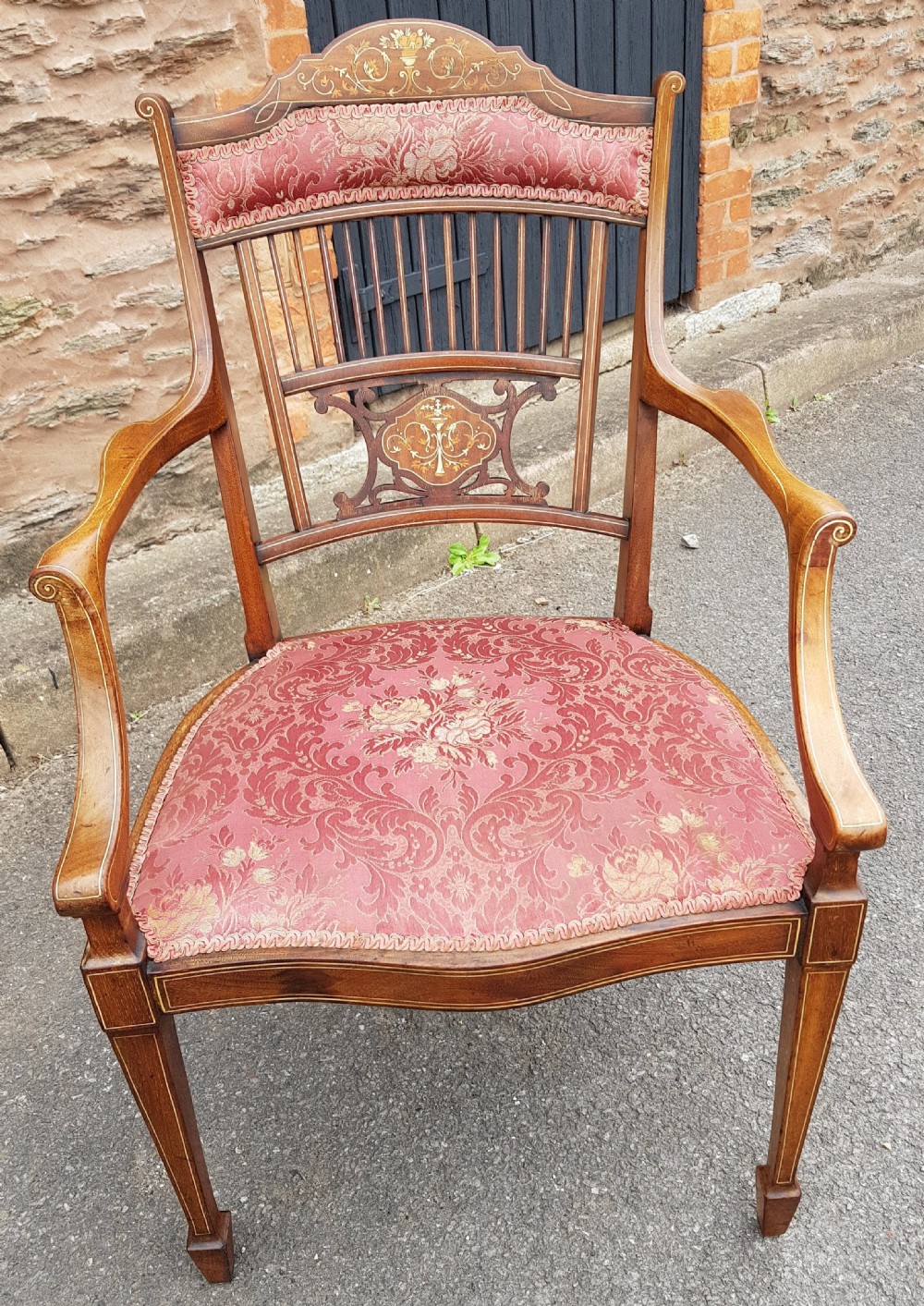 An Edwardian mahogany open armchair featuring floral marquetry inlay on the crest rail and central splat, swept armrests, and pink damask fabric upholstery.