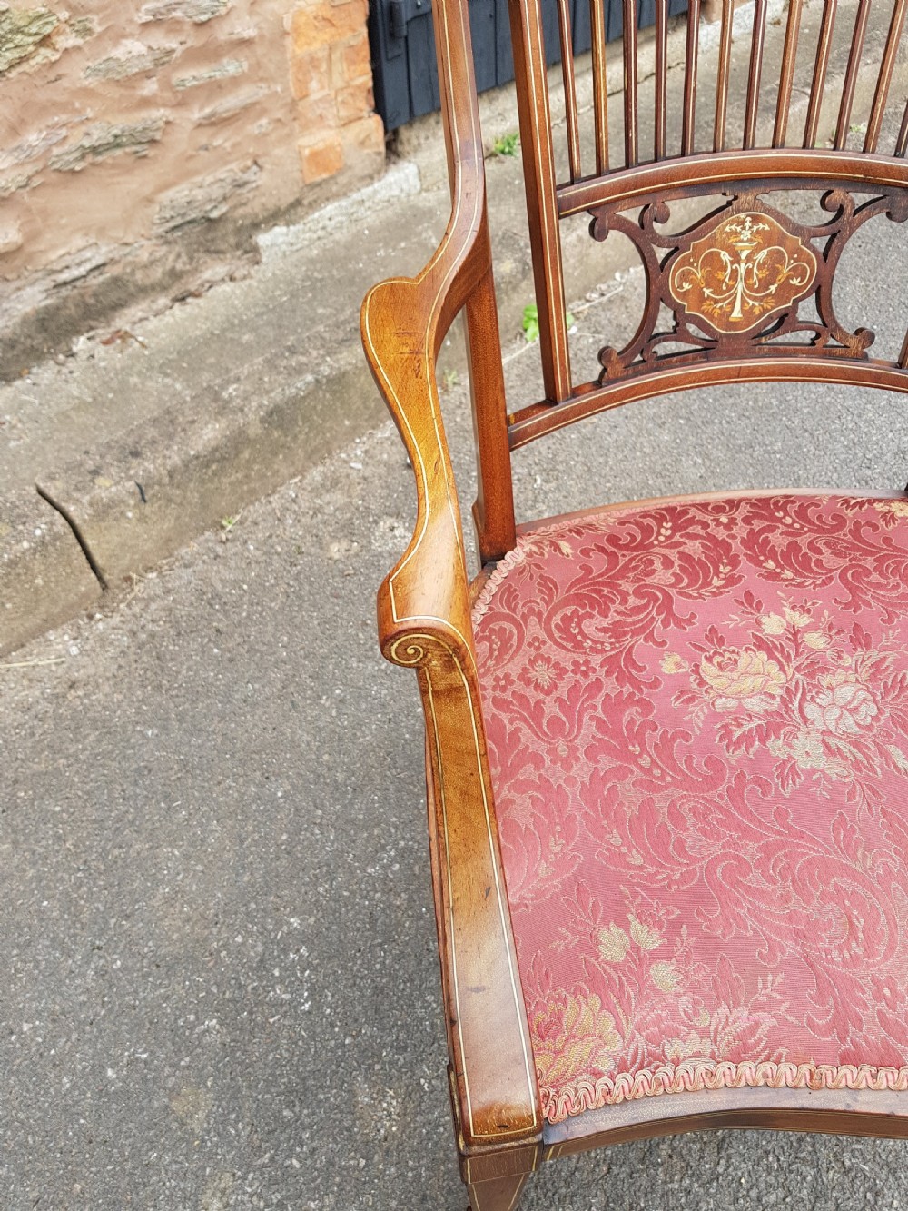 An Edwardian mahogany open armchair featuring floral marquetry inlay on the crest rail and central splat, swept armrests, and pink damask fabric upholstery. View V