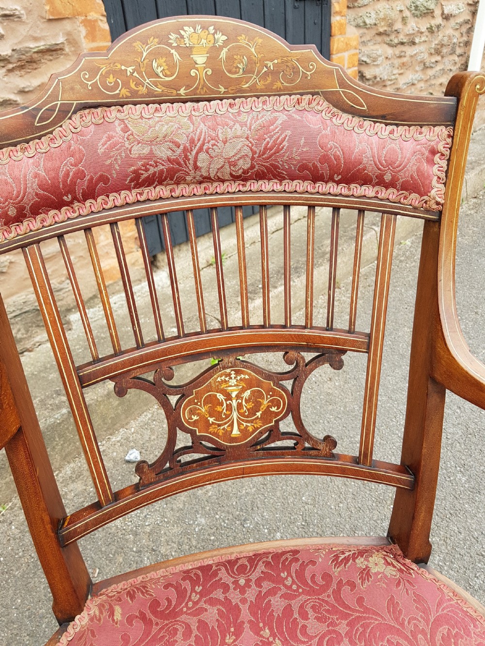 An Edwardian mahogany open armchair featuring floral marquetry inlay on the crest rail and central splat, swept armrests, and pink damask fabric upholstery. View VIII