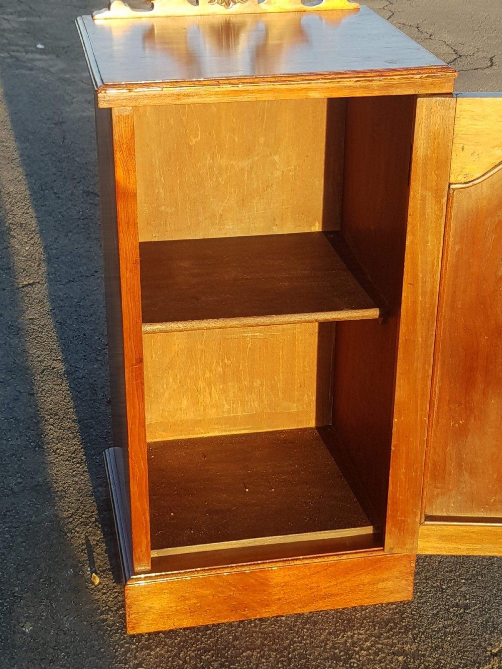 An Edwardian warm brown walnut bedside cabinet with a carved top gallery, single panel door with relief carving, brass drop handle, and plinth base. View IV