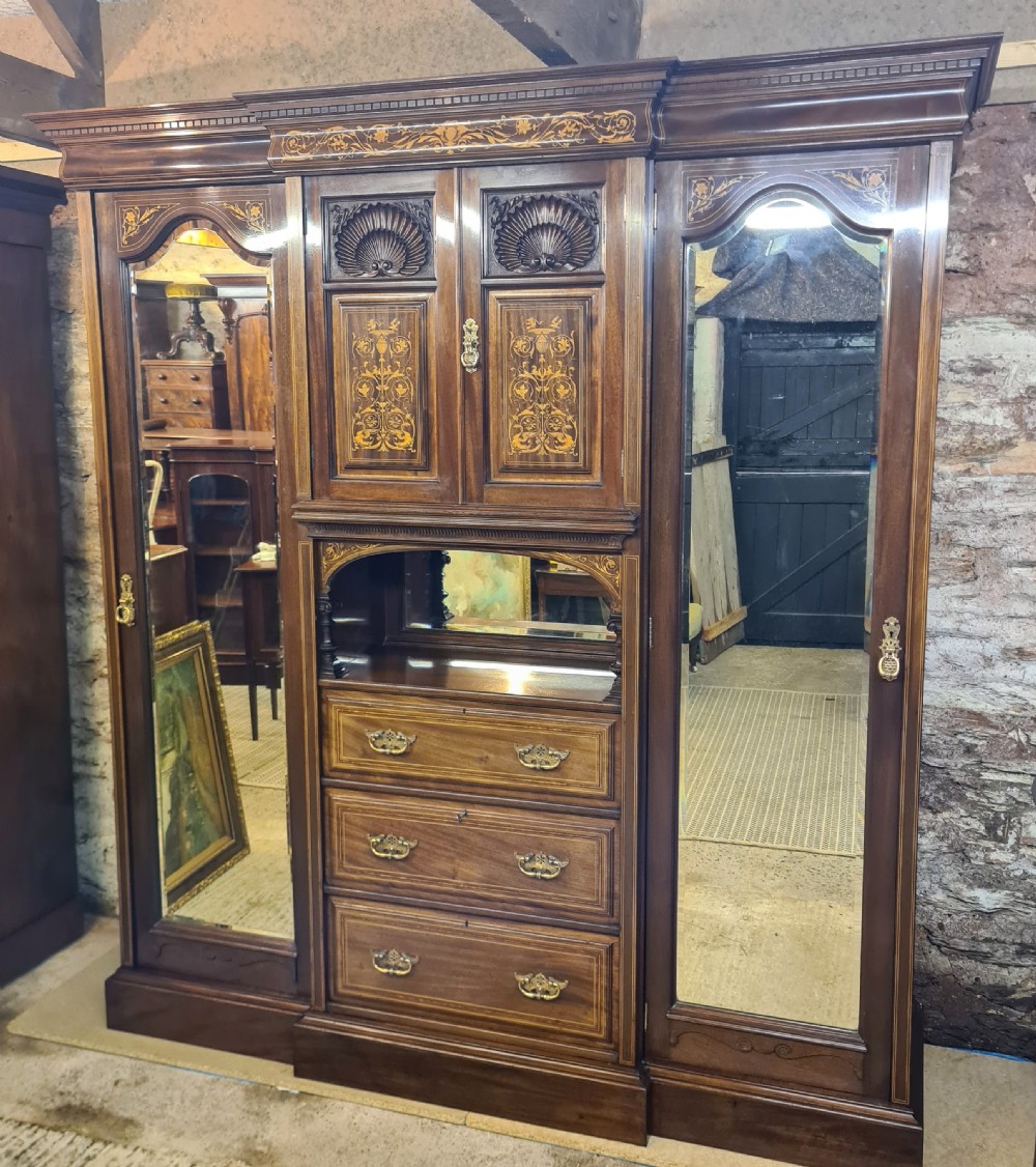 An Edwardian mahogany breakfront wardrobe with a central carved section, drawers, an open recessed shelf, and two full-length mirrored side doors.