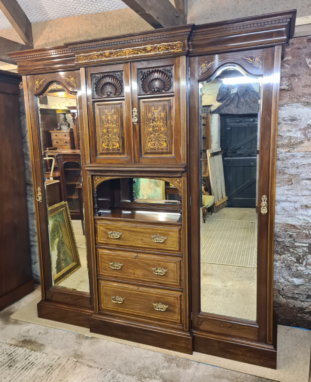 An Edwardian mahogany breakfront wardrobe with a central carved section, drawers, an open recessed shelf, and two full-length mirrored side doors. View II