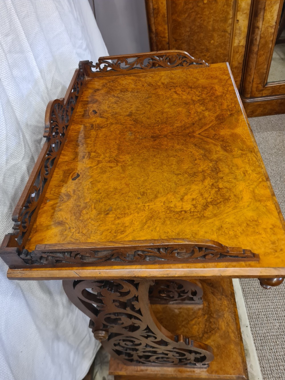 Victorian burr walnut Canterbury featuring intricate pierced fretwork dividers, an upper shelf with carved gallery, and turned legs on brass castors. View II