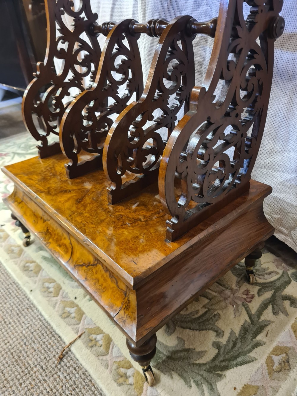 Victorian burr walnut Canterbury featuring intricate pierced fretwork dividers, an upper shelf with carved gallery, and turned legs on brass castors. View V
