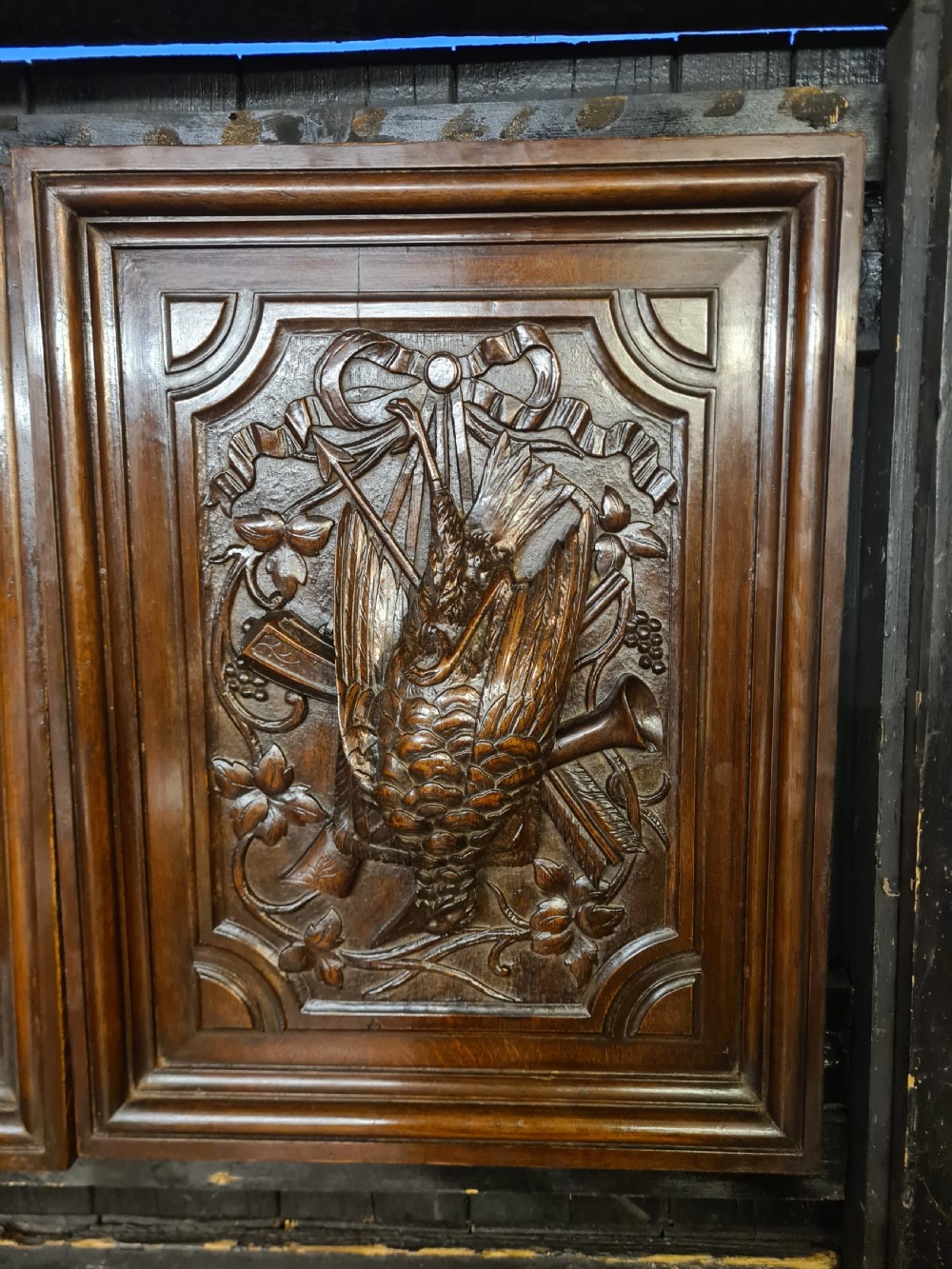 A pair of dark oak timber panels featuring high-relief relief carvings of game birds, a rabbit, ribbons, and hunting equipment. View II