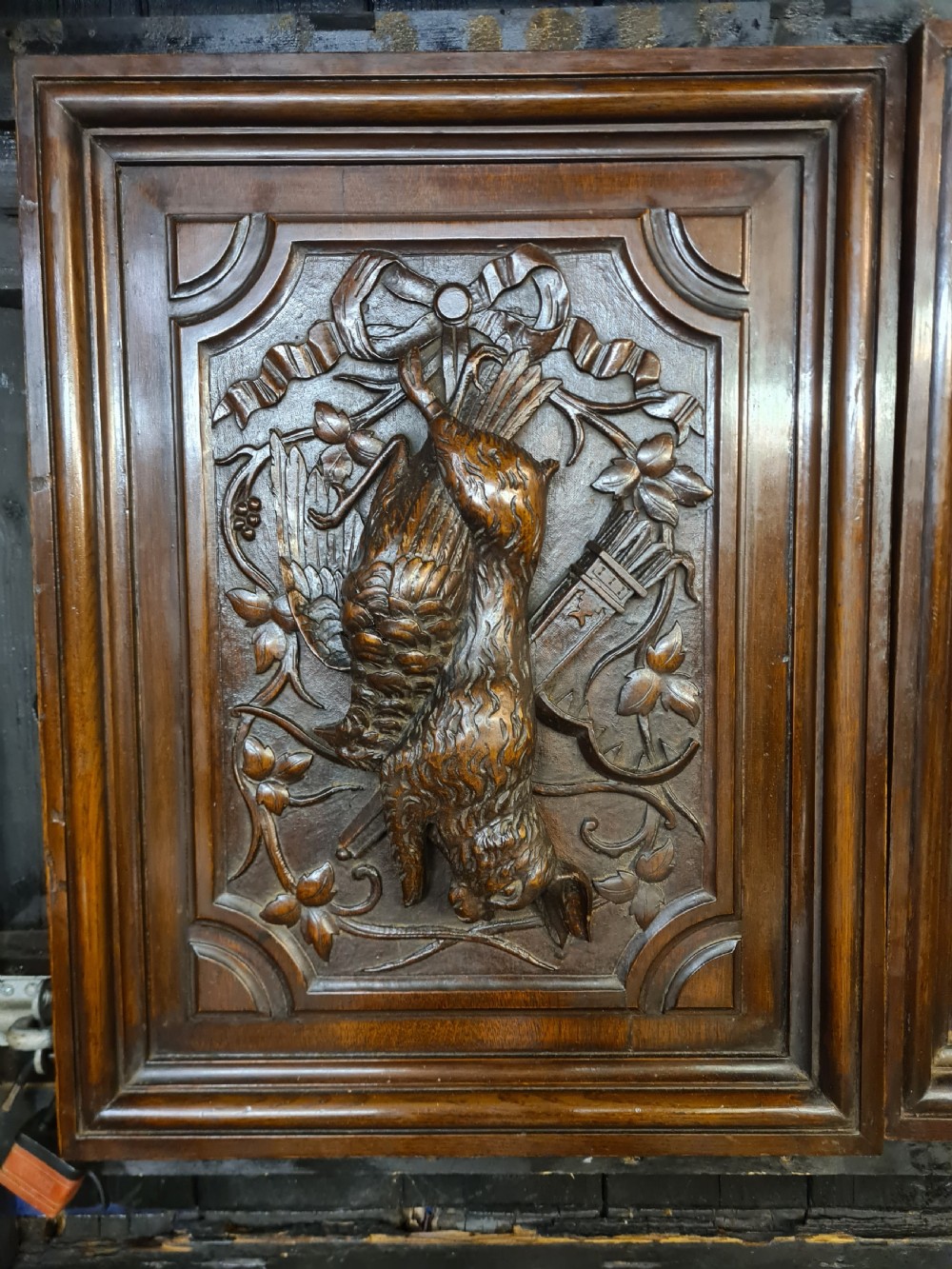 A pair of dark oak timber panels featuring high-relief relief carvings of game birds, a rabbit, ribbons, and hunting equipment. View III