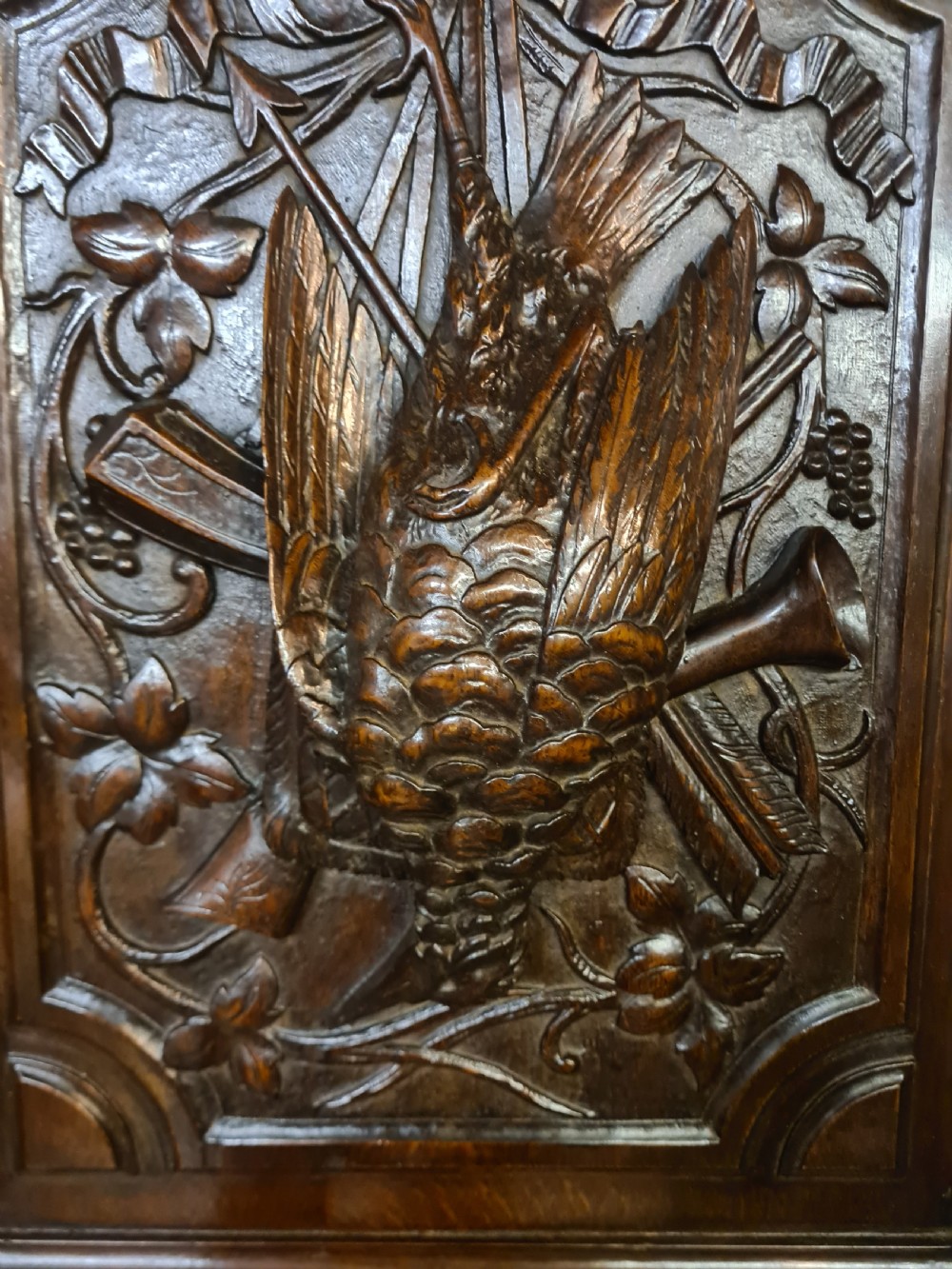 A pair of dark oak timber panels featuring high-relief relief carvings of game birds, a rabbit, ribbons, and hunting equipment. View V