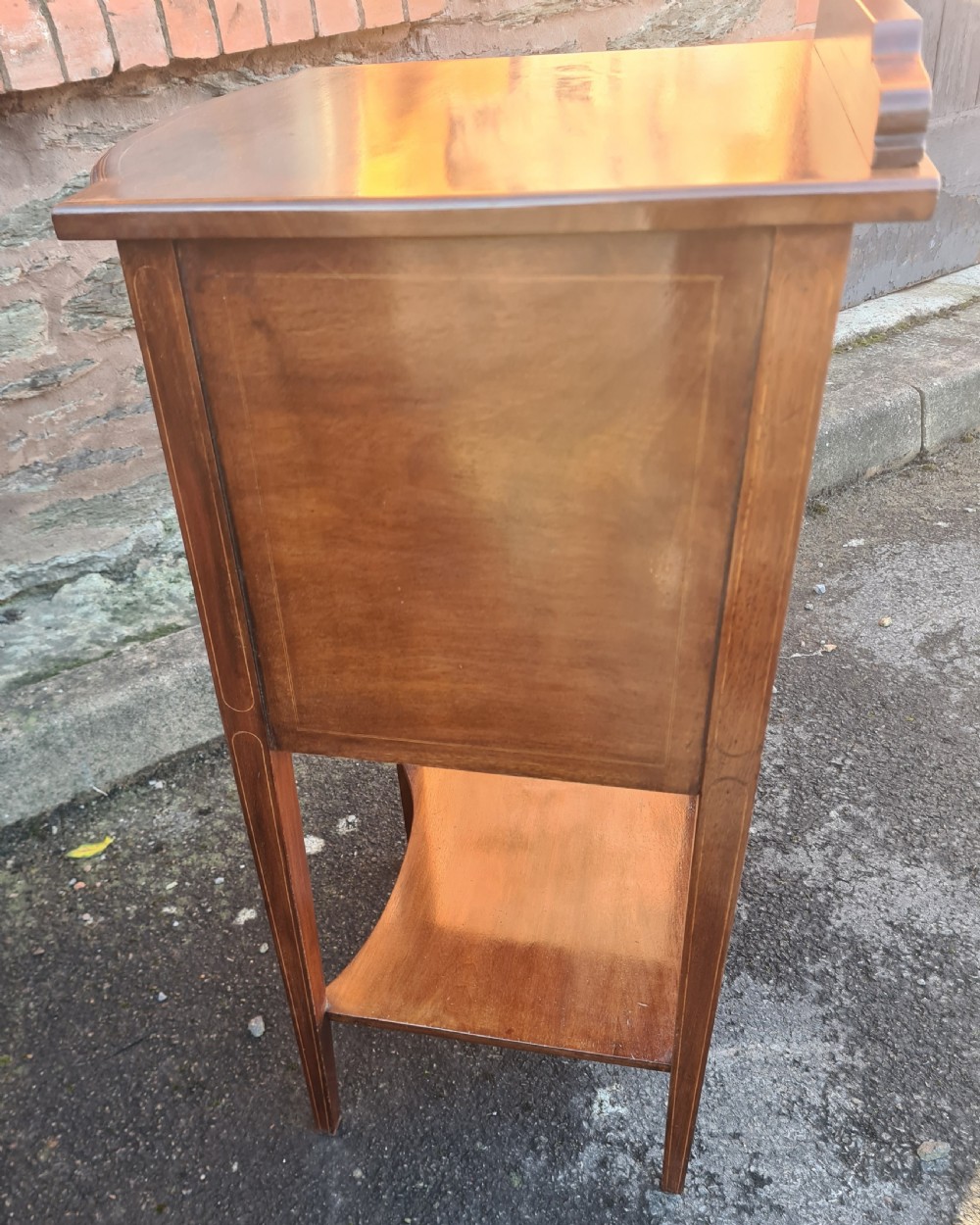 A 19th-century mahogany bedside cabinet featuring a bow-front cupboard door with inlay stringing, a brass handle, a lower shelf, and tapered square legs. View II