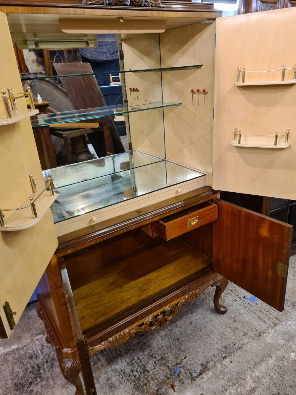 A two-door 1920s burr walnut cocktail cabinet featuring decorative brass strap hinges, book-matched wood grain, a carved apron, and cabriole legs. View VIII