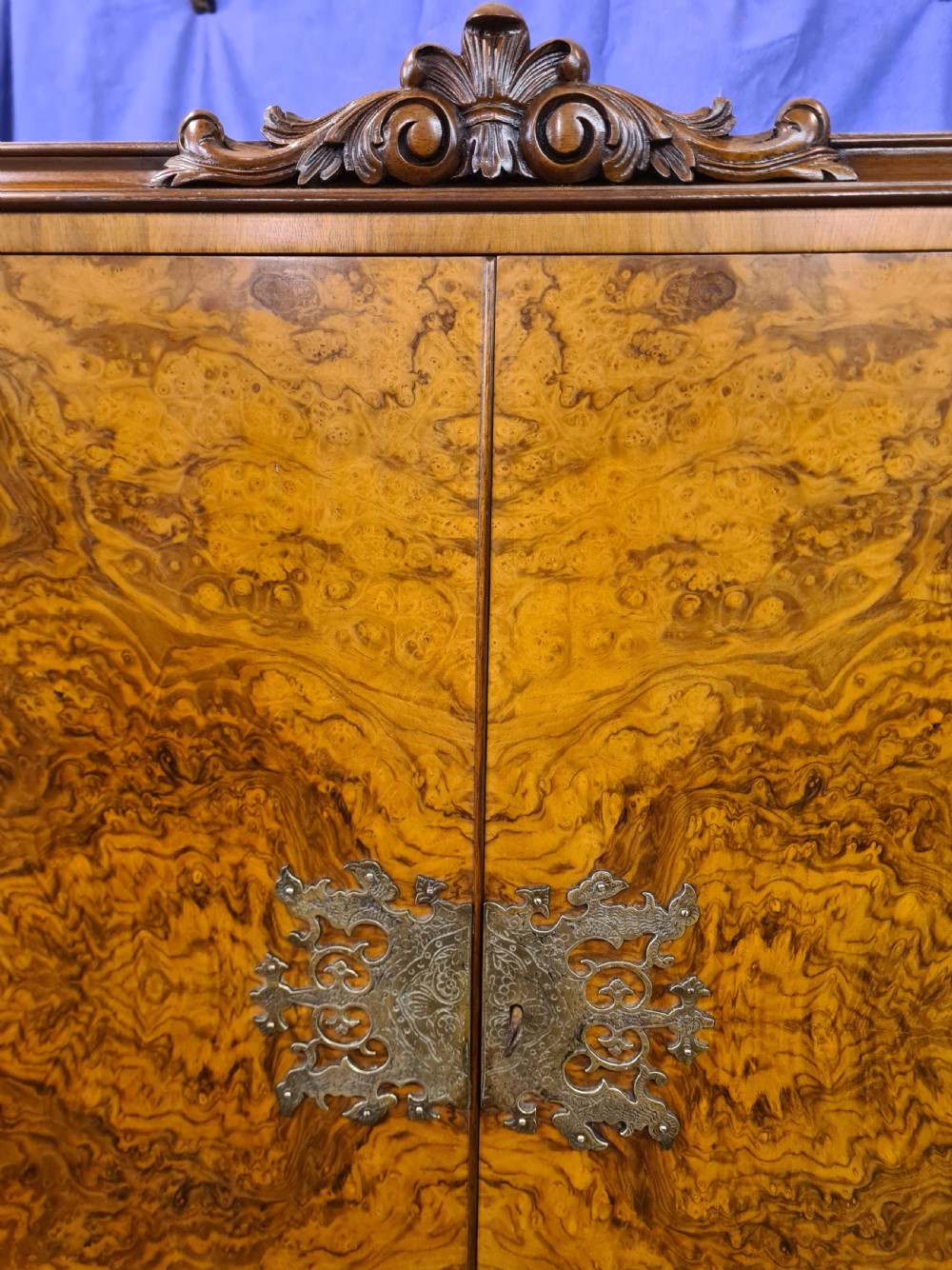 A two-door 1920s burr walnut cocktail cabinet featuring decorative brass strap hinges, book-matched wood grain, a carved apron, and cabriole legs. View IX