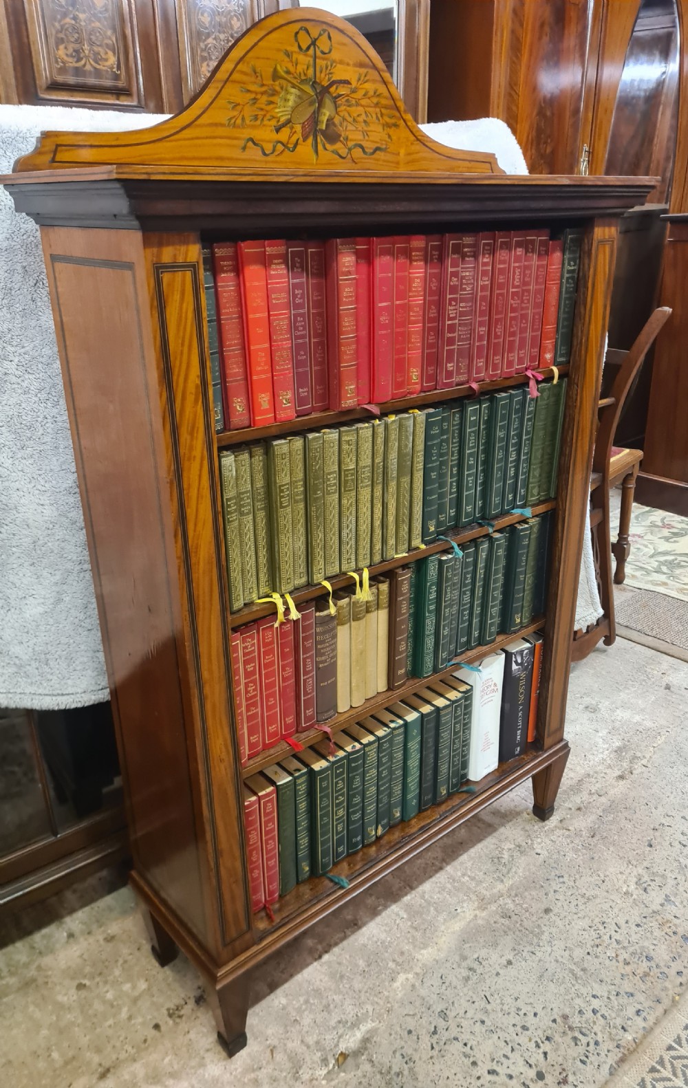 A Victorian satinwood open bookcase featuring four tiered shelves and an arched pediment decorated with marquetry foliage and musical instruments.
