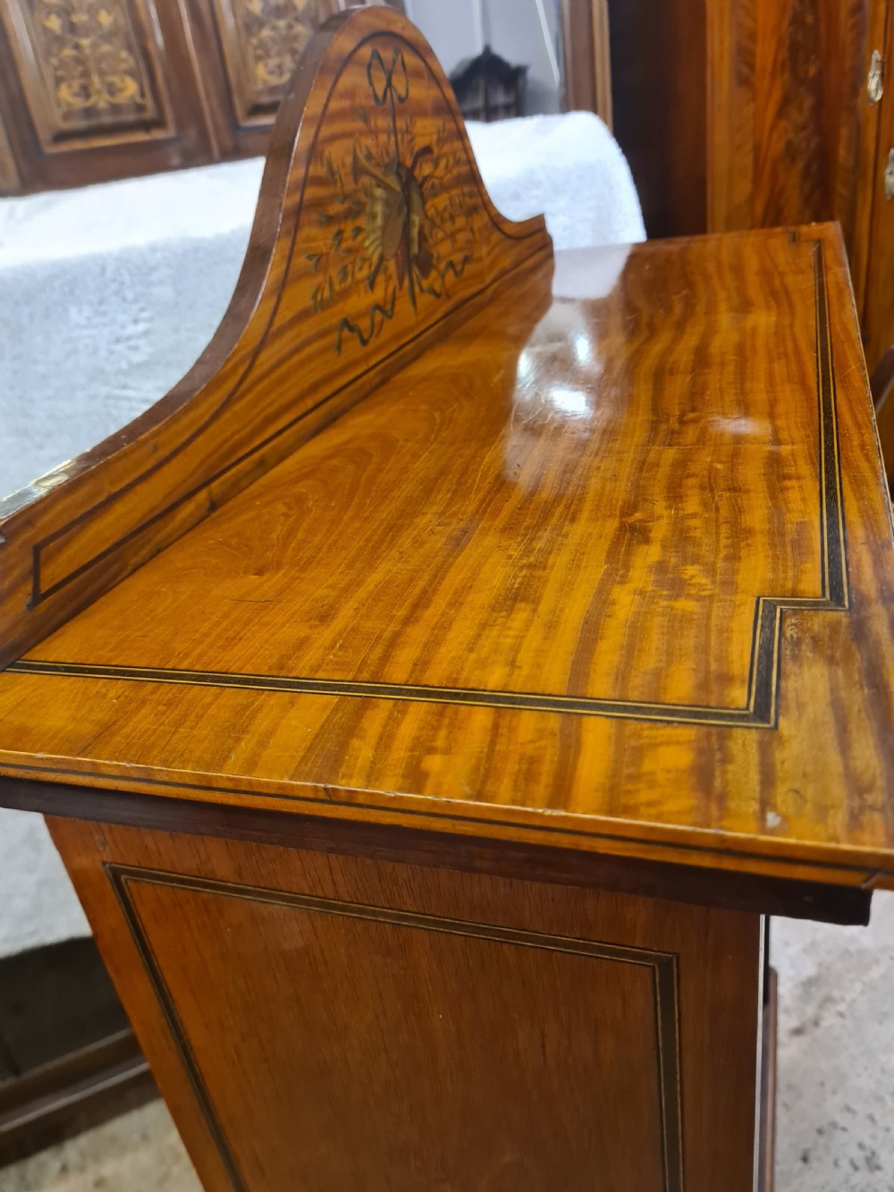 A Victorian satinwood open bookcase featuring four tiered shelves and an arched pediment decorated with marquetry foliage and musical instruments. View V