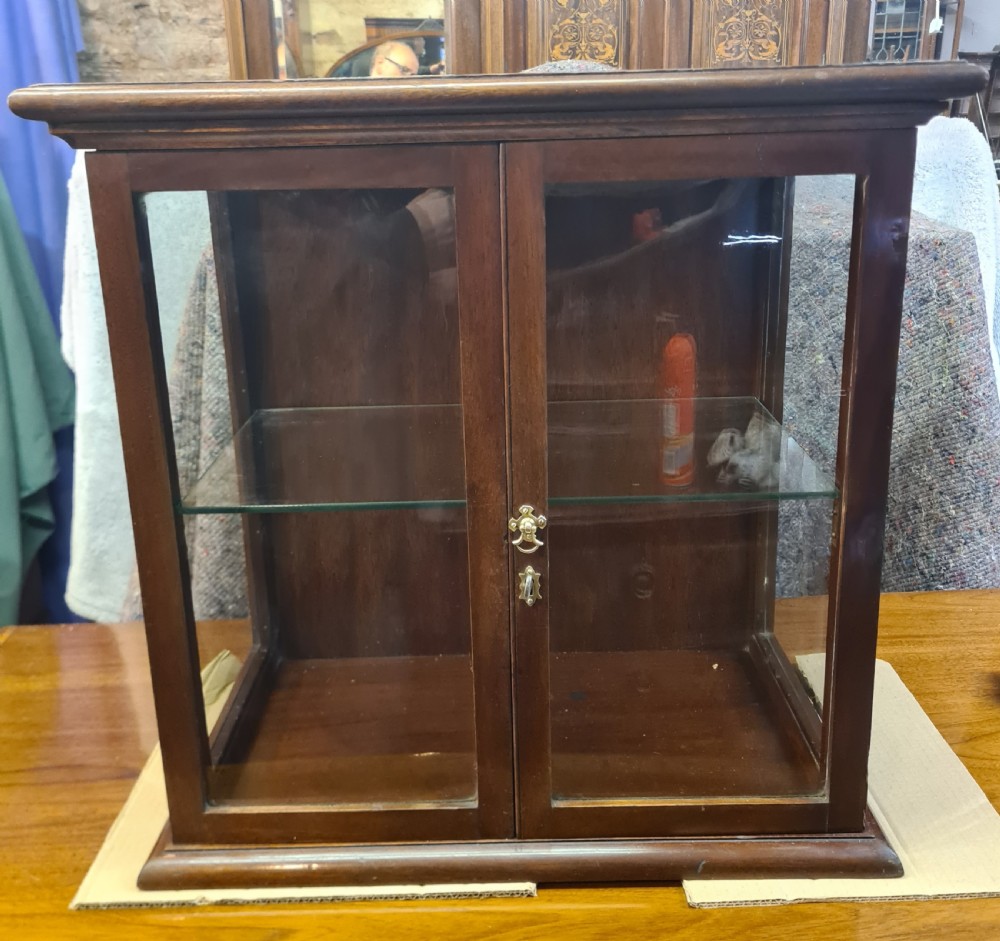 An Edwardian dark mahogany countertop display cabinet featuring twin glazed doors, side glass panels, a glass shelf, and a brass latch mechanism.