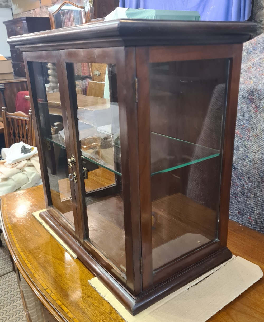 An Edwardian dark mahogany countertop display cabinet featuring twin glazed doors, side glass panels, a glass shelf, and a brass latch mechanism. View II