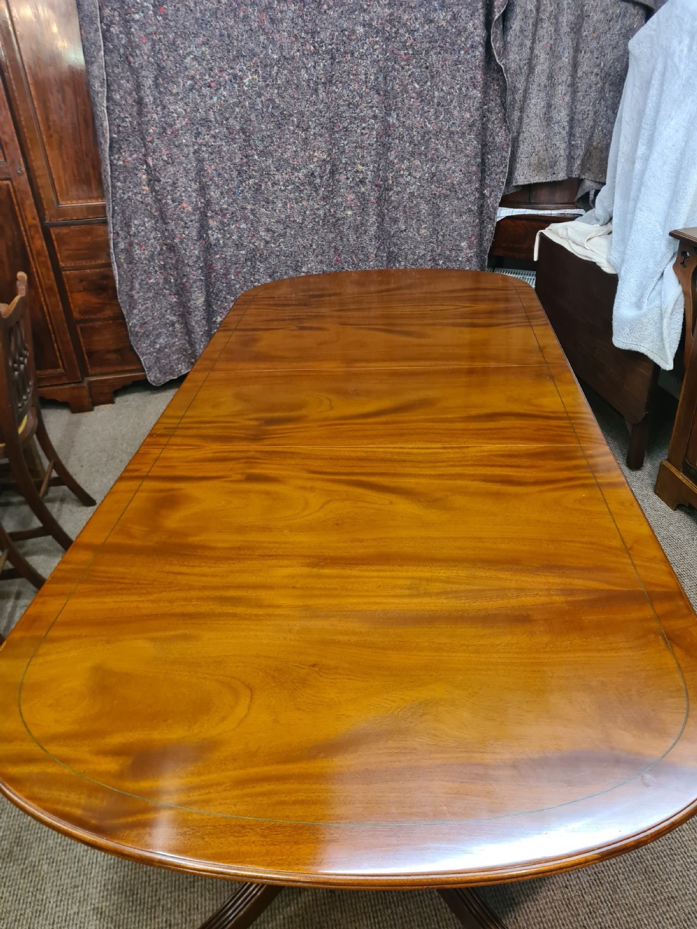 A polished warm brown mahogany dining table featuring fine brass inlay stringing around the perimeter with an inserted central leaf.