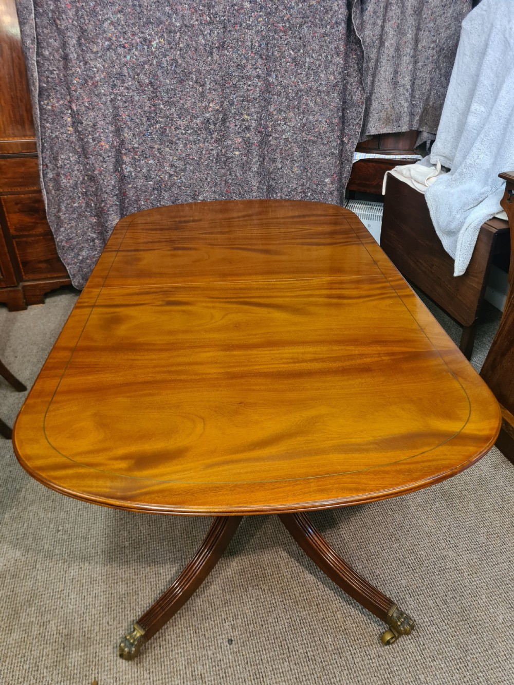 A polished warm brown mahogany dining table featuring fine brass inlay stringing around the perimeter with an inserted central leaf. View II