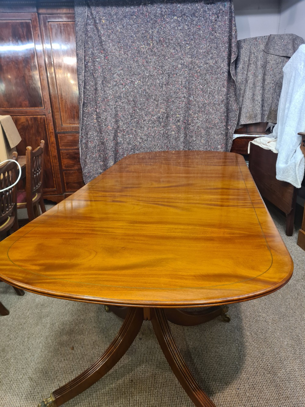 A polished warm brown mahogany dining table featuring fine brass inlay stringing around the perimeter with an inserted central leaf. View IV