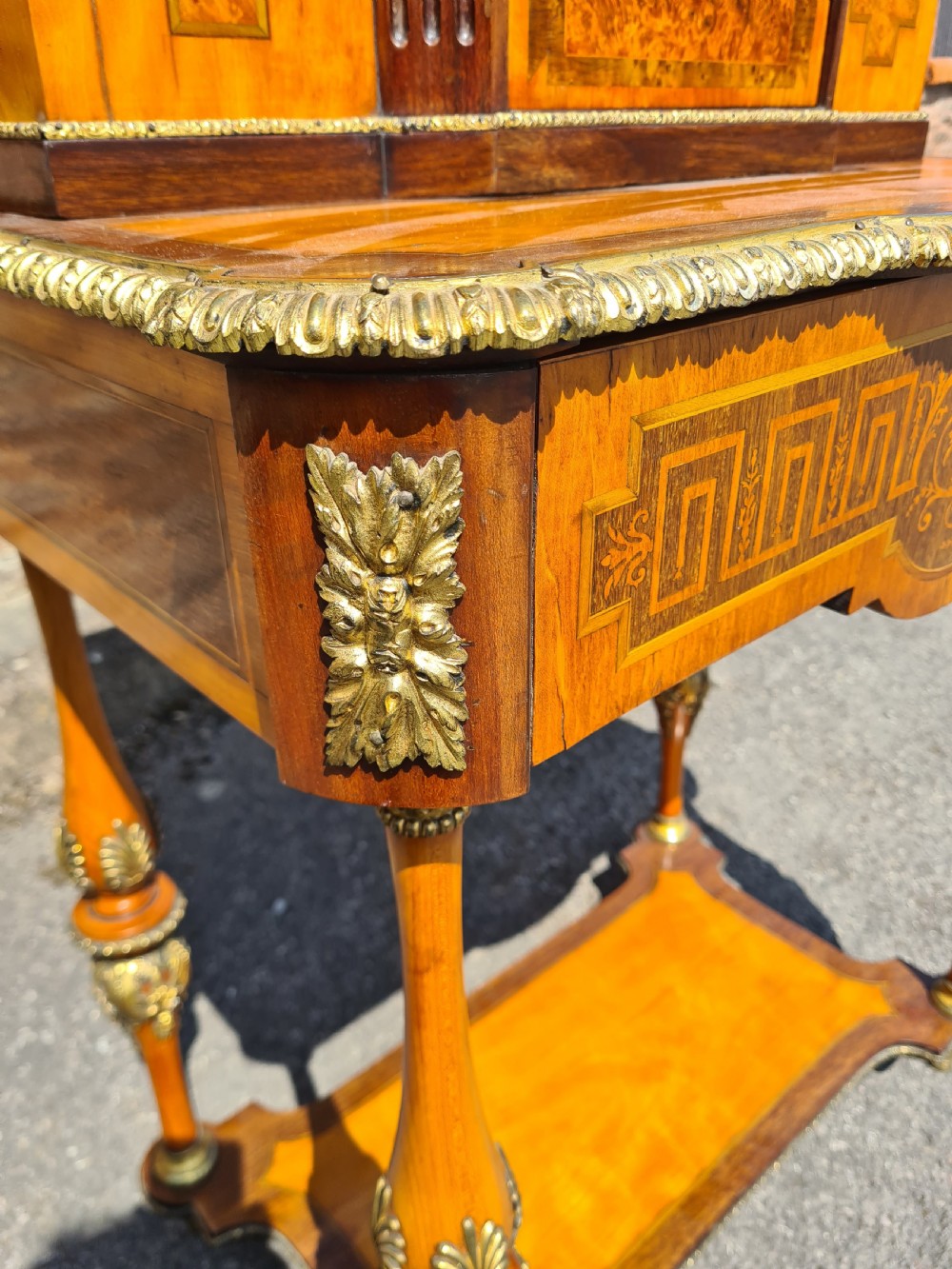 A French satinwood and amboyna bonheur de jour desk featuring ornate gilt-bronze mounts, an inlaid Greek key drawer pattern, and a central cabinet door set with a hand-painted porcelain portrait plaque. View V