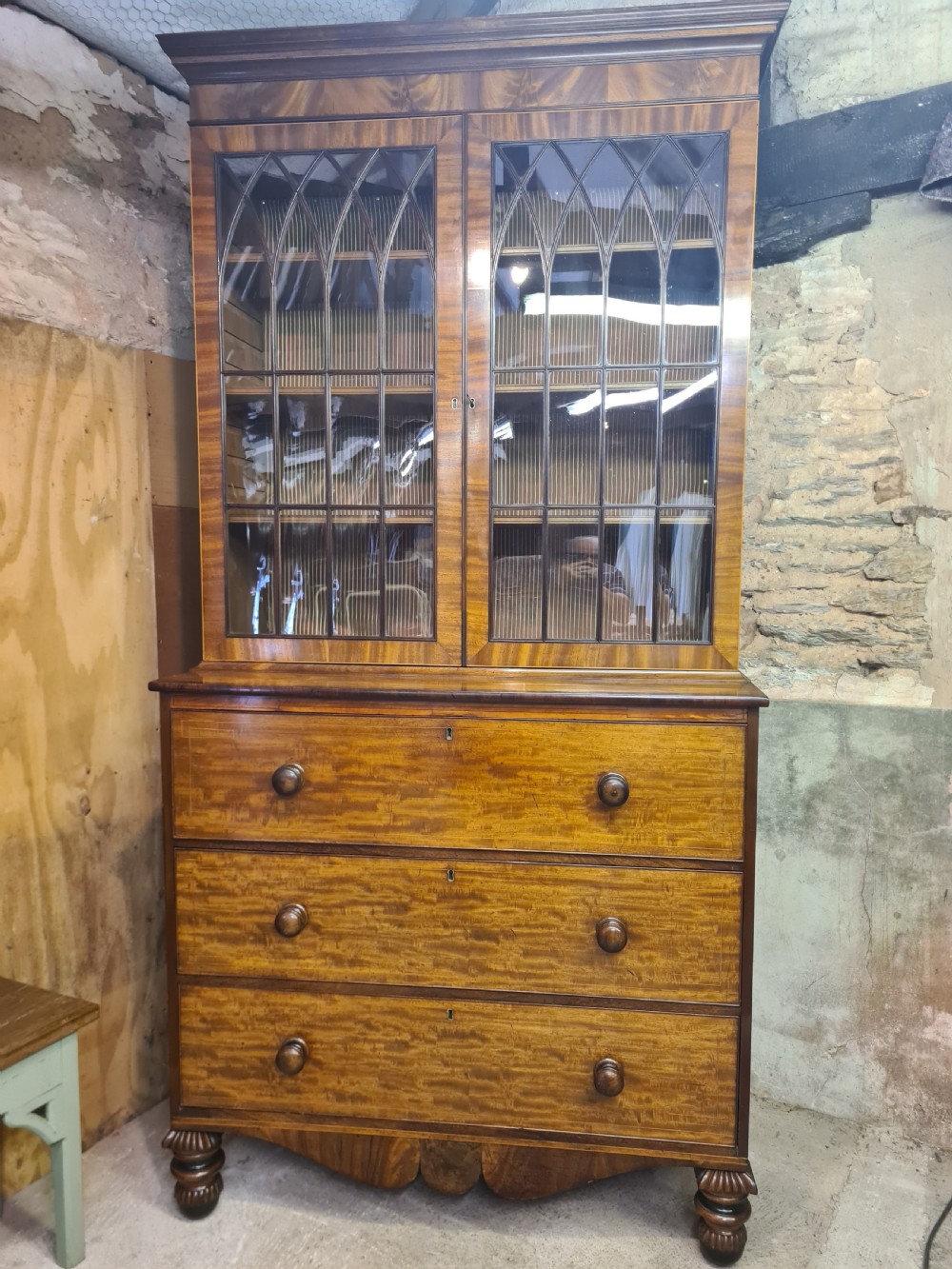 A nineteenth-century mahogany secretaire bookcase featuring an upper cabinet with twin astragal glazed doors above a lower chest with three drawer fronts set on turned feet. View II