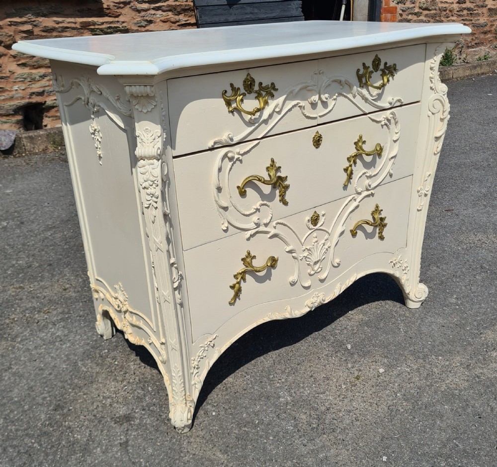 An off-white 19th-century Rococo style painted commode with a shaped white marble top, three drawers, foliate relief carving, and gilt brass handles. View II