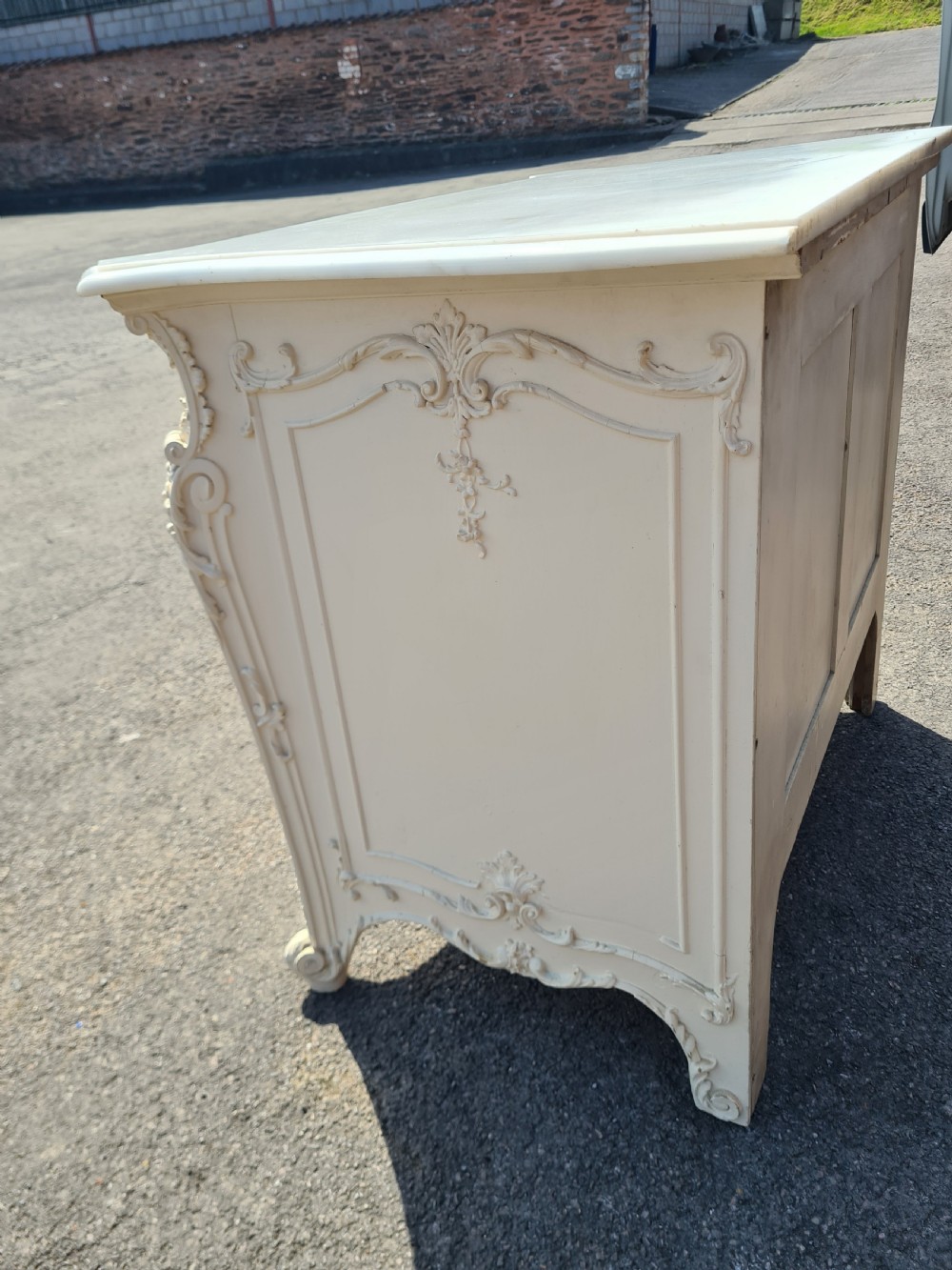 An off-white 19th-century Rococo style painted commode with a shaped white marble top, three drawers, foliate relief carving, and gilt brass handles. View V