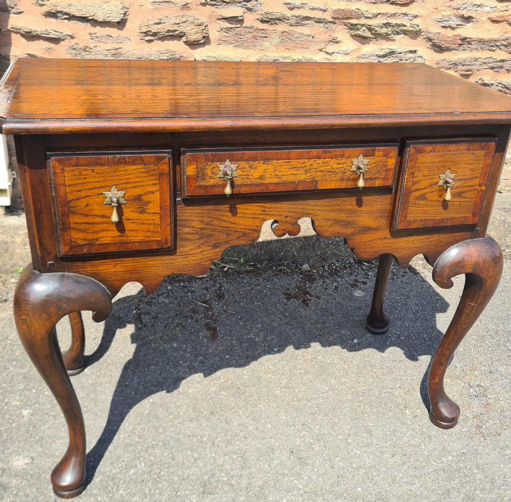 A 1920s Georgian style oak lowboy featuring three drawers with brass drop handles, a shaped lower apron, and four cabriole legs ending in pad feet.