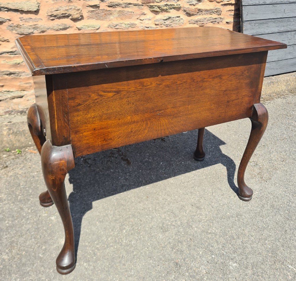 A 1920s Georgian style oak lowboy featuring three drawers with brass drop handles, a shaped lower apron, and four cabriole legs ending in pad feet. View V