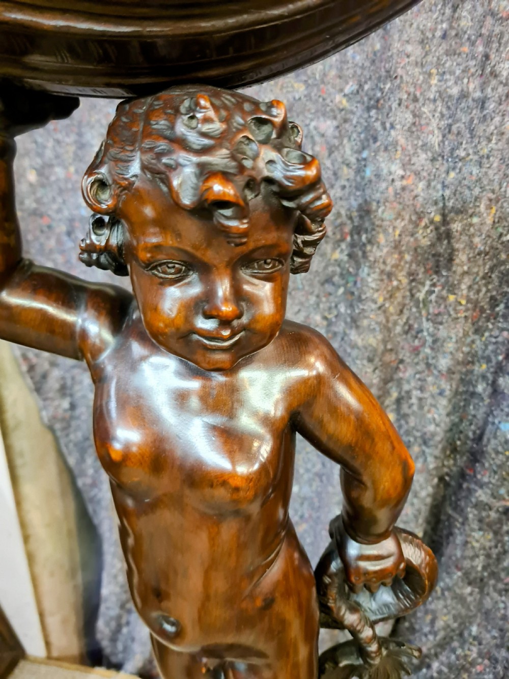 A 19th-century carved dark lime wood sculpture of a putto holding a shell basin aloft, standing on an ornate scroll-carved pedestal. View VI