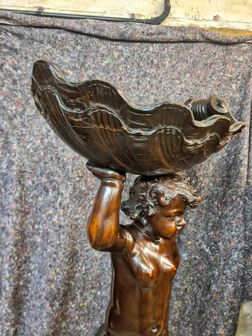 A 19th-century carved dark lime wood sculpture of a putto holding a shell basin aloft, standing on an ornate scroll-carved pedestal. View VII
