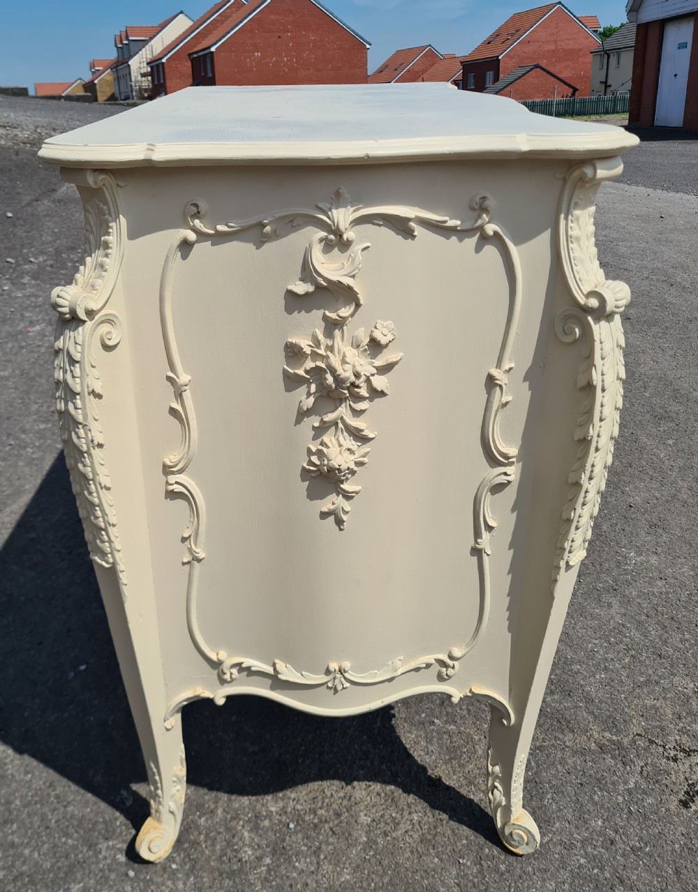 A nineteenth-century cream painted serpentine commode featuring three drawers with rococo style relief carvings and brass handles. View II