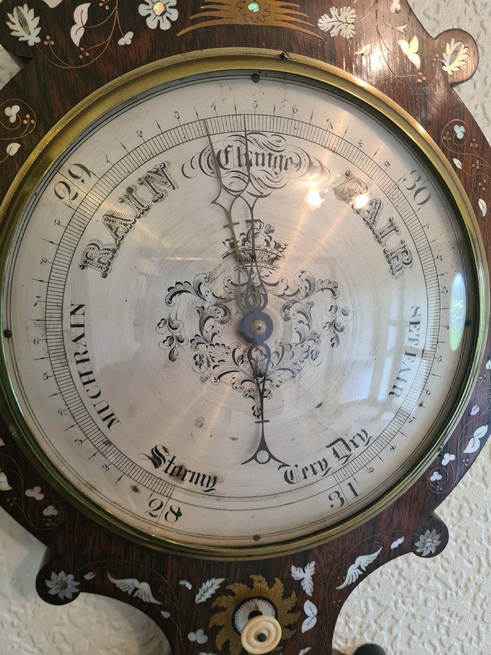 A 19th-century dark rosewood banjo barometer featuring intricate mother-of-pearl floral and bird inlays, an integrated thermometer, and a central round silvered dial. View V