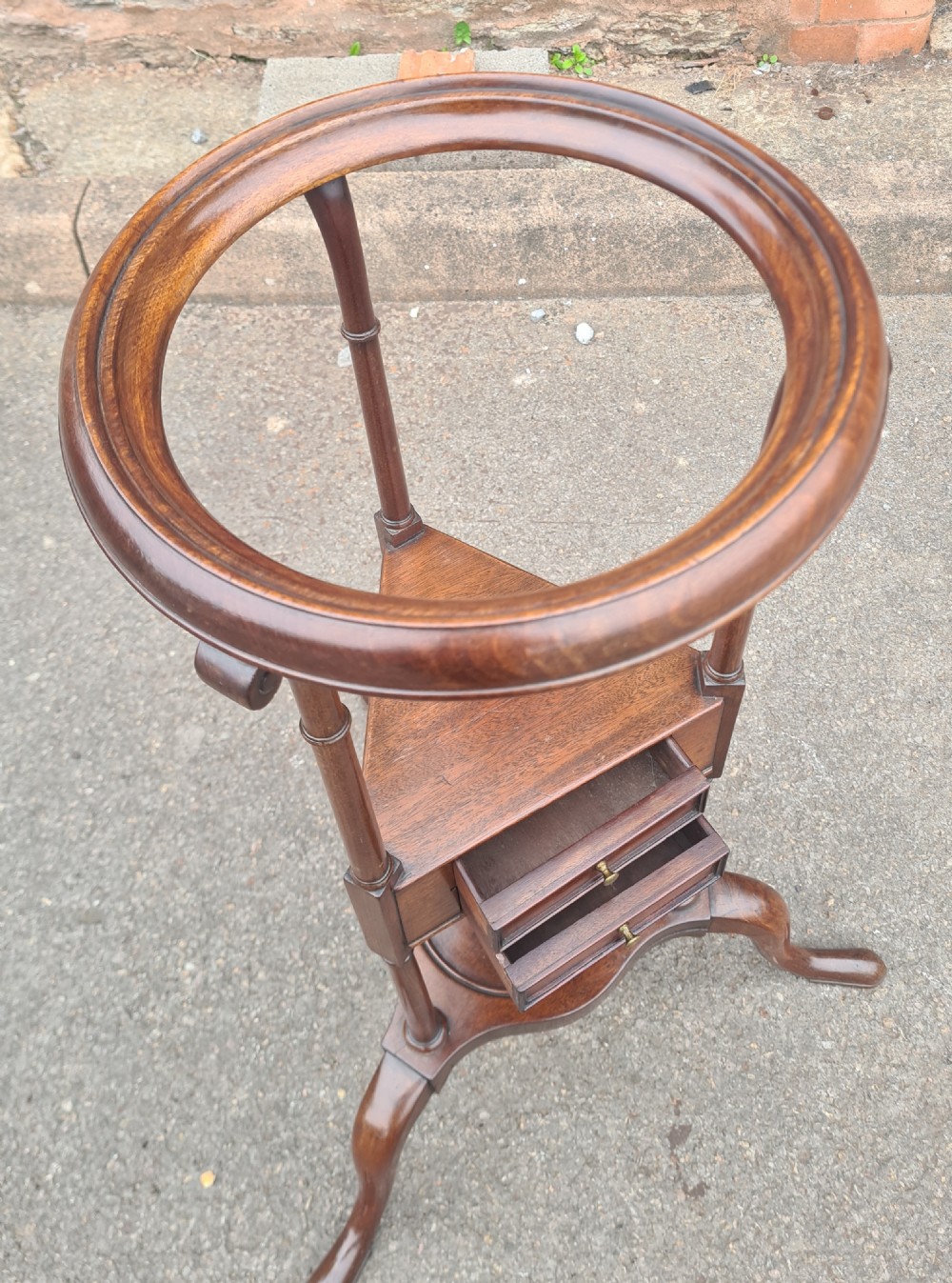 A Georgian mahogany tripod wig stand featuring a circular dished top rim, central triangular drawer unit with brass pulls, turned supports, and cabriole legs. View III
