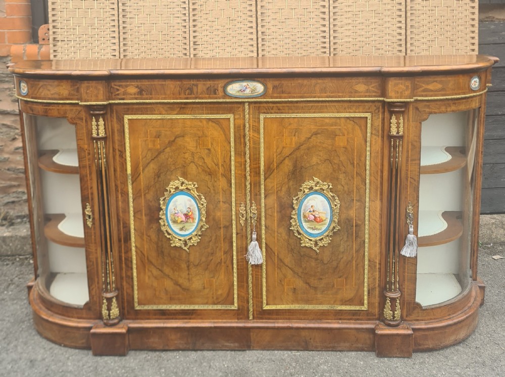 A Victorian burr walnut credenza with central timber doors framed in ormolu, featuring oval Sevres-style porcelain plaques and curved glass display cabinets on each side.