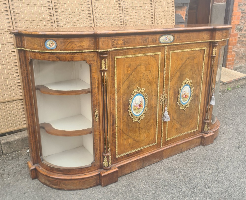 A Victorian burr walnut credenza with central timber doors framed in ormolu, featuring oval Sevres-style porcelain plaques and curved glass display cabinets on each side. View II