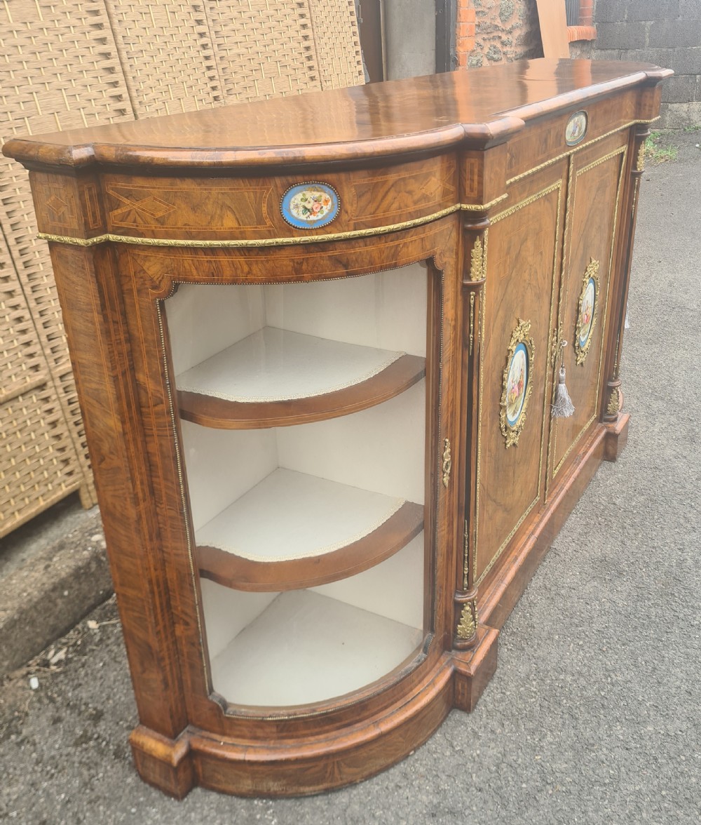 A Victorian burr walnut credenza with central timber doors framed in ormolu, featuring oval Sevres-style porcelain plaques and curved glass display cabinets on each side. View VI