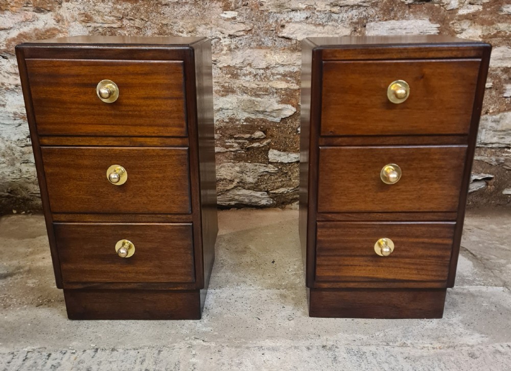 A pair of mahogany Art Deco bedside cabinets featuring three drawers each with round brass knobs on a solid plinth base.