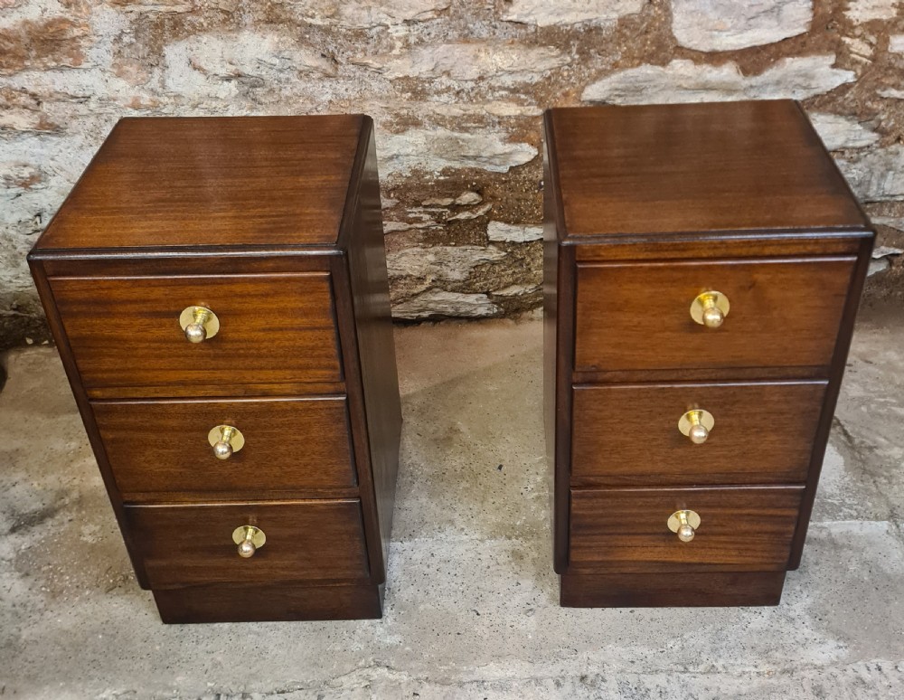 A pair of mahogany Art Deco bedside cabinets featuring three drawers each with round brass knobs on a solid plinth base. View II
