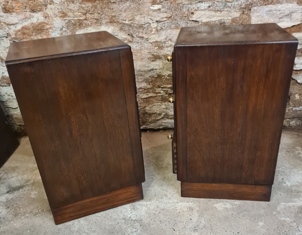 A pair of mahogany Art Deco bedside cabinets featuring three drawers each with round brass knobs on a solid plinth base. View III