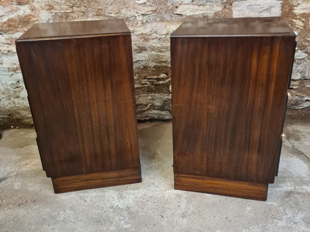 A pair of mahogany Art Deco bedside cabinets featuring three drawers each with round brass knobs on a solid plinth base. View IV