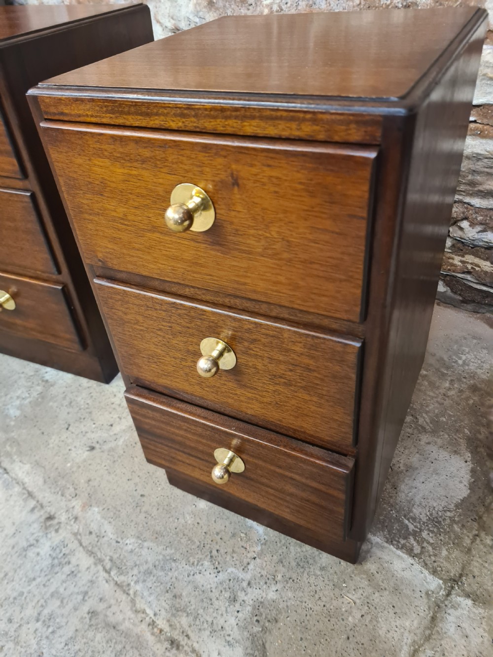 A pair of mahogany Art Deco bedside cabinets featuring three drawers each with round brass knobs on a solid plinth base. View V