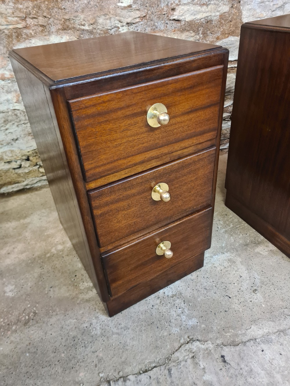 A pair of mahogany Art Deco bedside cabinets featuring three drawers each with round brass knobs on a solid plinth base. View VI