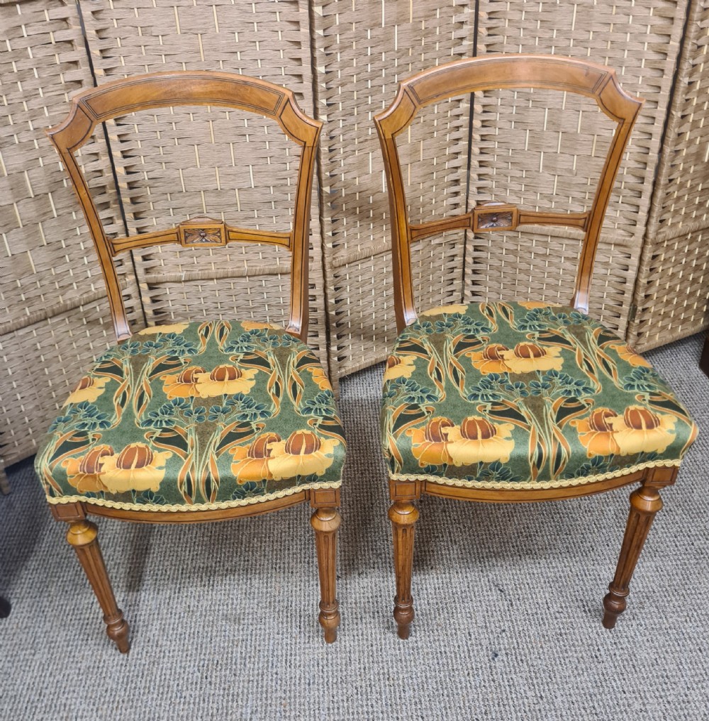 A pair of 19th-century satinwood side chairs featuring inlaid frames, open backs, turned fluted legs, and green floral pattern upholstery.
