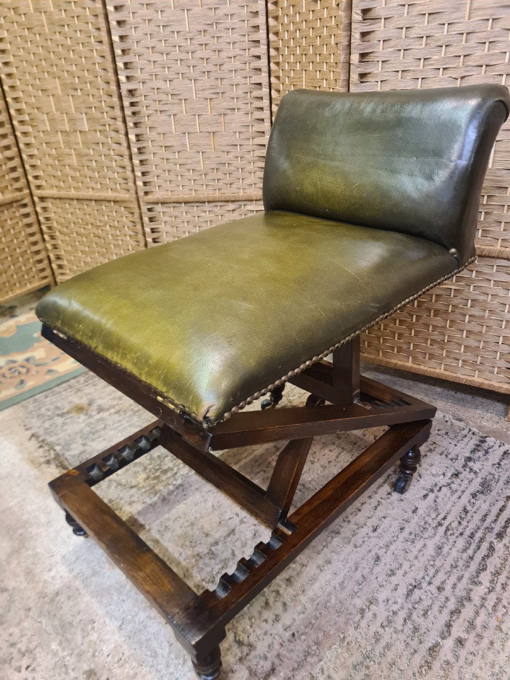 An Edwardian metamorphic gout stool crafted from dark mahogany with green leather upholstery, brass stud detailing, and a notched ratchet adjustment mechanism.