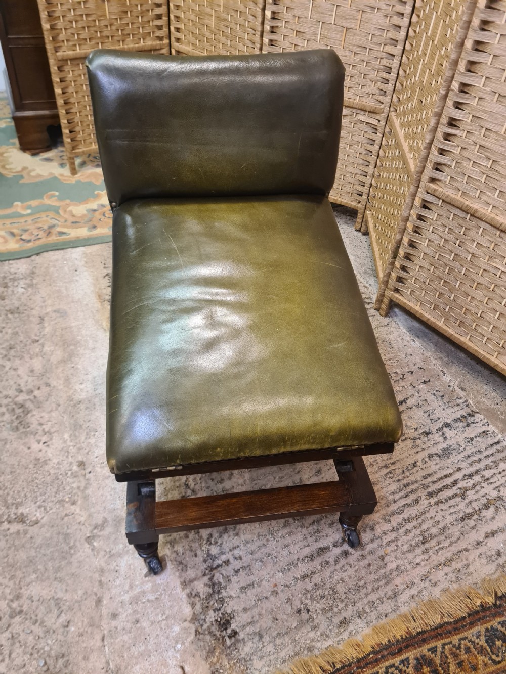 An Edwardian metamorphic gout stool crafted from dark mahogany with green leather upholstery, brass stud detailing, and a notched ratchet adjustment mechanism. View V