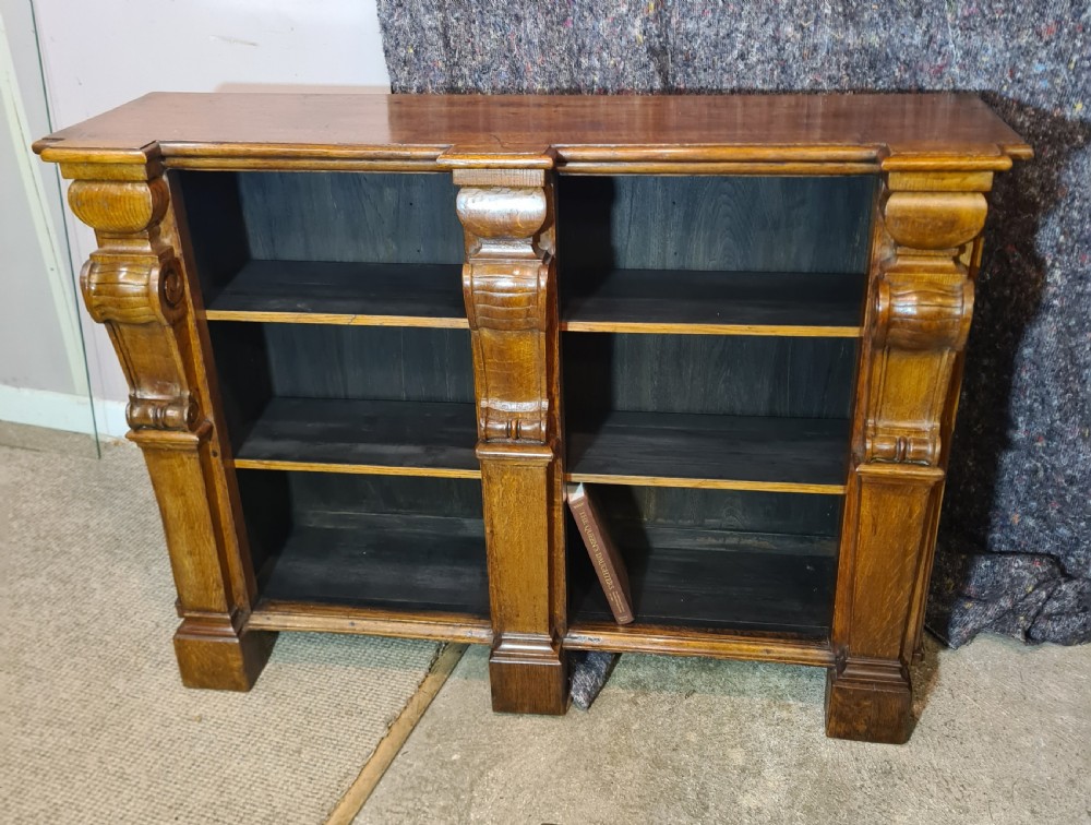 A low 19th-century open double bookcase made of dark stained oak with heavy carved corbels flanking two bays of shelves.