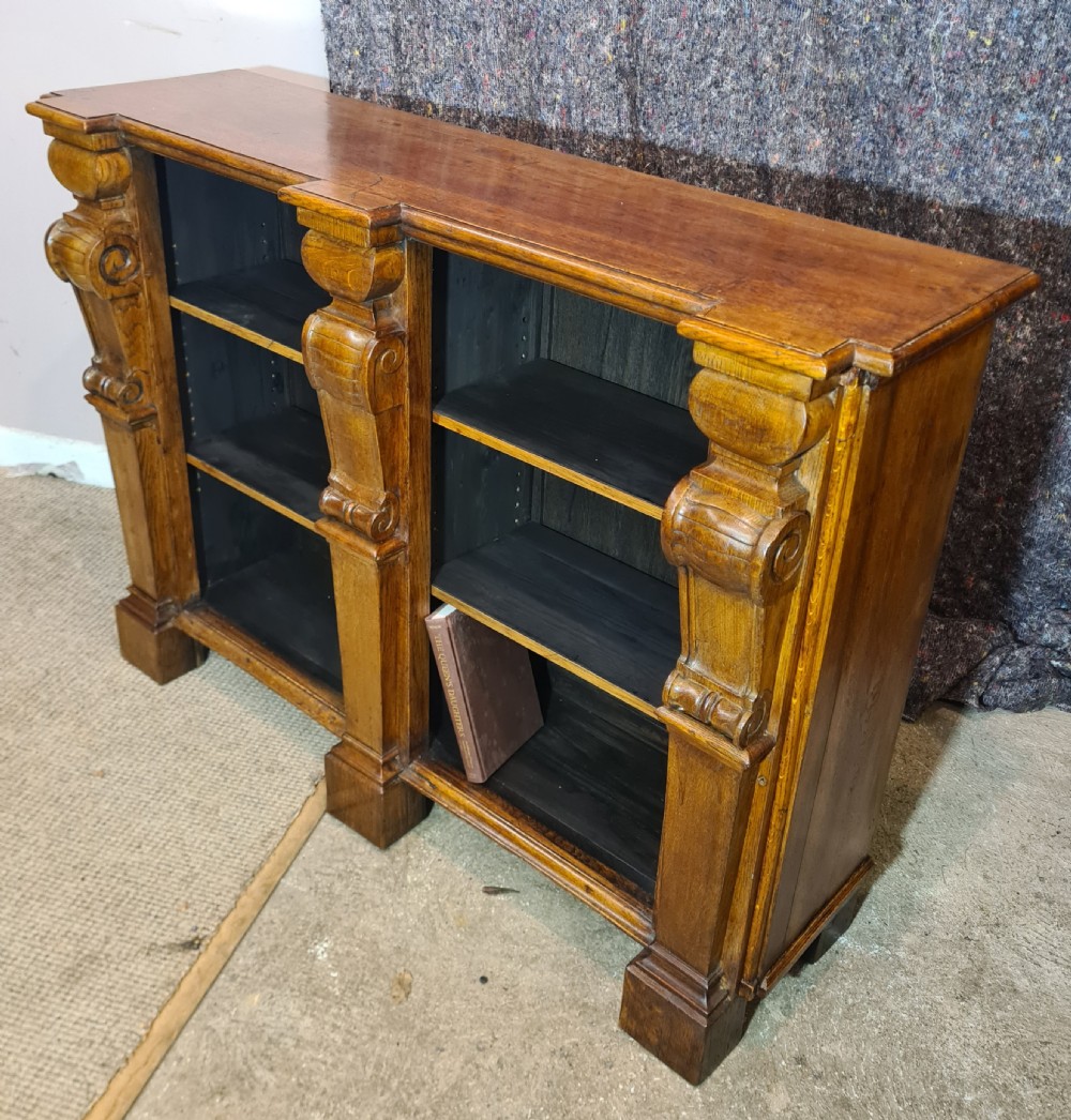 A low 19th-century open double bookcase made of dark stained oak with heavy carved corbels flanking two bays of shelves. View II