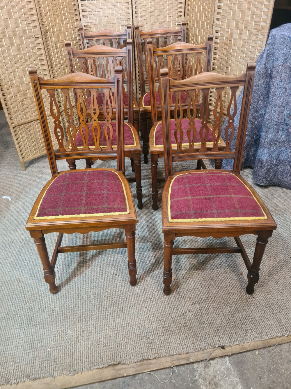 Set of six walnut Arts and Crafts dining chairs featuring pierced back slats, turned front legs, and red tartan upholstered seats with yellow trim.