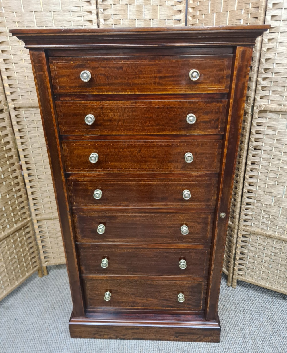 A tall, narrow late Victorian mahogany Wellington chest featuring seven drawers with satinwood stringing inlays, round brass knobs, and a side locking bar.