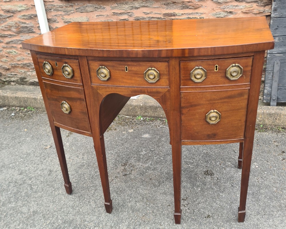 A Georgian mahogany bowfront sideboard featuring a curved front, octagonal brass handles, three drawers, and four square tapered legs.